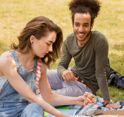 Sudents boy and girl having picnic eating pizza. Summer day in campus, students having picnic.