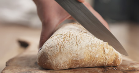 Wall Mural - young female hands slicing ciabatta with olives on cutting board