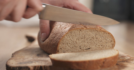 Wall Mural - young female hands slicing rye wheat rustic bread on cutting board