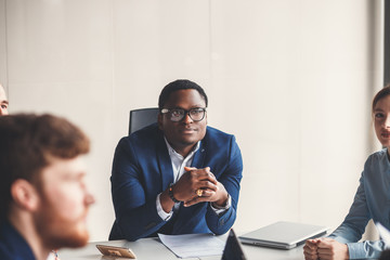 Portrait of smiling pretty young african business man in glasses sitting on workplace