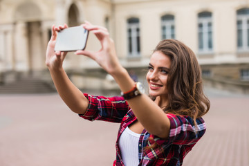 Wall Mural - Young girl take selfie from hands with phone on summer city street urban life concept