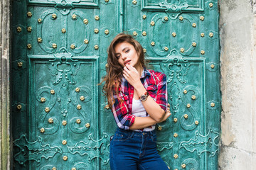 Wall Mural - close up portrait of cute smiling woman on a background of green vintage door wearing casual clothes in summer city