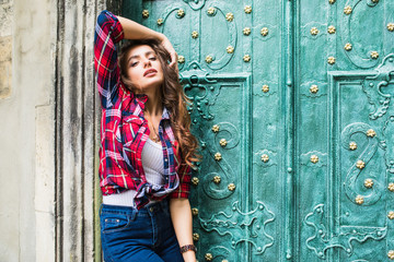 Wall Mural - close up portrait of cute smiling woman on a background of green vintage door wearing casual clothes in summer city