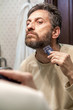 © glebchik - Grooming beard. Man alone shears beard in bathroom