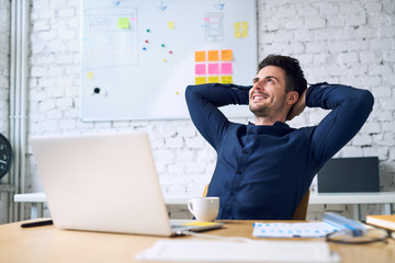 Smiling handsome businessman relaxing and enjoying coffee while taking break from work in office