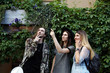 © shurkin_son - People, friendship, summer holidays and tourism concept. Three stylish teenagers standing at green wall and pointing index fingers up, looking excited while having walk in resort town during vacations