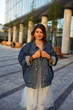 © shurkin_son - People, youth, modern urban lifestyle, fashion and style concept. Happy stylish teenage girl wearing trendy accessories and denim jacket over elegant dress, standing in cityscape, smiling at camera