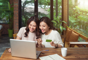 Happy relaxed young female friends doing online shopping through laptop and credit card at home