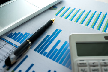 Close up of business pen and white calculator on financial graph data with laptop. finance, saving, investment, business and banking concept