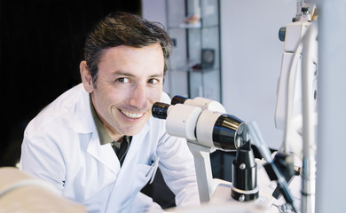 Portrait of handsome eye doctor sitting with ophthalmologic device in the cabinet