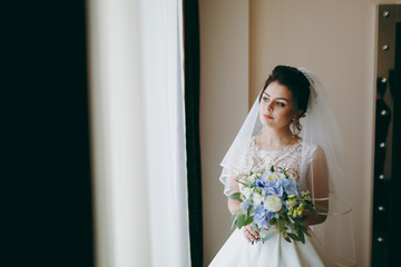 Wall Mural - Beautiful bride stands with a bouquet near the window