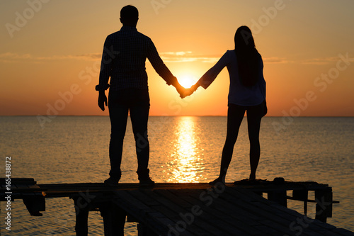 images Sunset Two People Holding Hands Silhouette https stock adobe com images silhouette of two young people guy and girl on a wooden bridge holding hands looking out to the sea at sunset 165438872 start checkout 1 content id 165438872