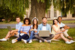 © deagreez - It`s more easy together! Six cheerful classmates are sitting on plaid on the green grass in spring park near campus and study, preparing for exams, tests, looking in camera and smiling