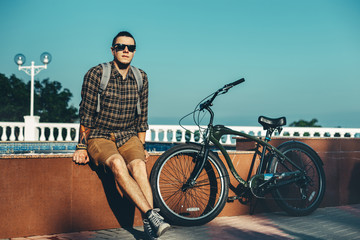 Wall Mural - Young Man In Sunglasses Sitting On Fountain Next To Bicycle In Summer Park Daily Lifestyle Urban Resting Concept