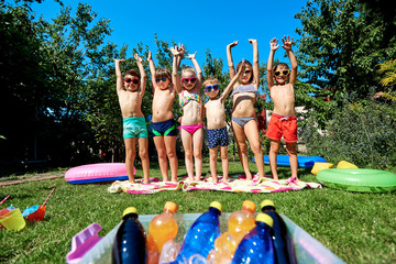 Group of children in swimsuit with arms raised on grass in summer.