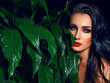 Beautiful sultry tanned girl with bright make-up and dark hair. She is in the jungle among the leaves. Cosmetics, spa, health, relaxation.