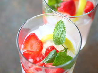 Two glasses of fruit water with fresh strawberries, lemon and mint over crushed ice