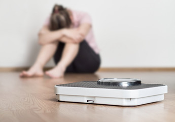 weight loss fail concept. scale and depressed, frustrated and sad woman sitting on floor holding hea