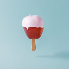 Red apple with ice cream stick on pastel blue background. Food creative concept.