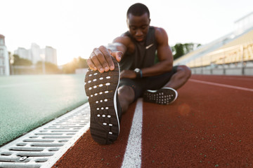 young concentrated african male athlete stretching legs