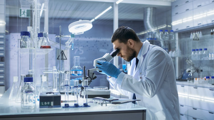 research scientist looks into microscope. he's conducts experiments in modern laboratory.