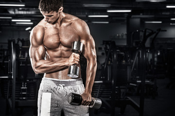  Athletic shirtless young sports man - fitness model holds the dumbbell in gym. Copy space fore your text.