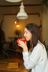 Wall Mural - Red cup of coffee in the hands of a beautiful smiling girl