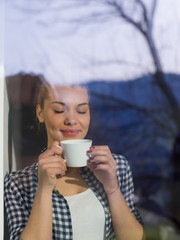 Wall Mural - young woman drinking morning coffee by the window