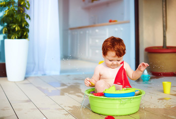 cute redhead toddler baby having fun with water on summer terrace