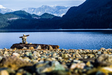 Inukshuk On Rocky Shore With Mountains And Lake