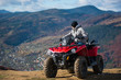 © anatoliy_gleb - Man in winter clothes on a red quad bike on a mountain top enjoying the view of the mighty mountains behind him. Blurred background of mountain scenery