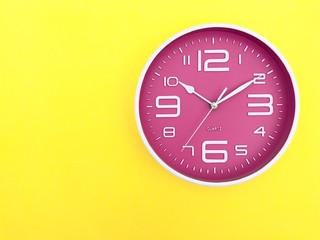 Wall Mural - Closeup A pink wall clock set on yellow background. Top view with Copy space. Selective focus.