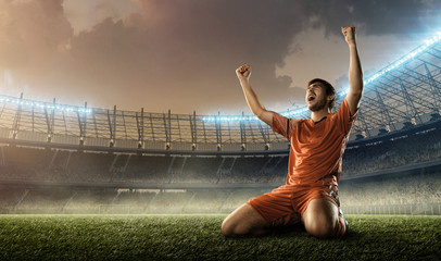 soccer player in red uniform celebrates a goal on a soccer stadium holding hands above his head and screaming