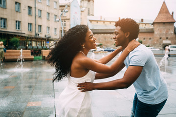 Positive emotional photo of amazing young africam american couple whirling and hugging over city square with fountain on background. Travel recreation lifestyle, water fountain.