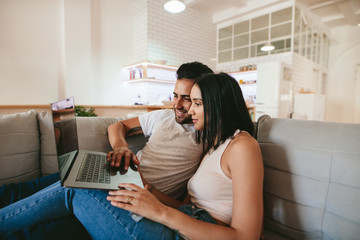 Wall Mural - Young couple relaxing on couch with laptop