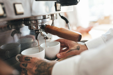 Close up barista hands making coffee by coffee machine in restaurant. Man hands holding two white cups and preparing coffee in coffee machine at cafe