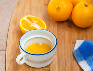 A blue edge cup with orange juice, whole and cut orange fruits on a wooden background.