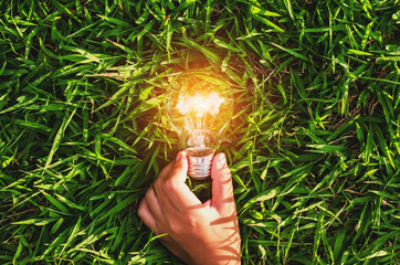 Wall Mural - hand hold light bulb on grass with sunset power energy concept nature