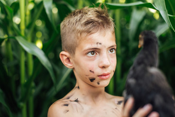 Little boy holding chick near village with blur background