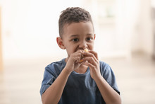 Cute Little Boy Eating Piece Of Bread On Blurred Background. Poverty Concept