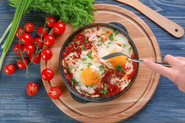 Poster - Woman eating eggs in purgatory on wooden background