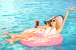 © Africa Studio - Beautiful young woman with glass of cocktail relaxing on inflatable donut in pool