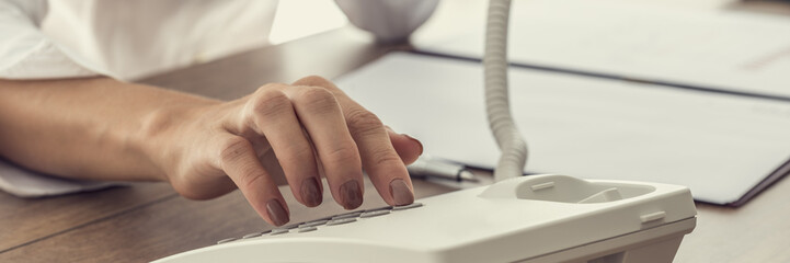 Woman dialing a telephone number on white landline phone