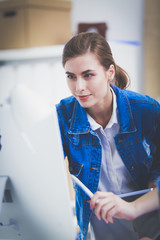 Two young woman standing near desk with instruments, plan and laptop.