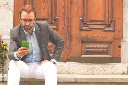 Fotografía Young modern man in suit using cellphone outdoors.