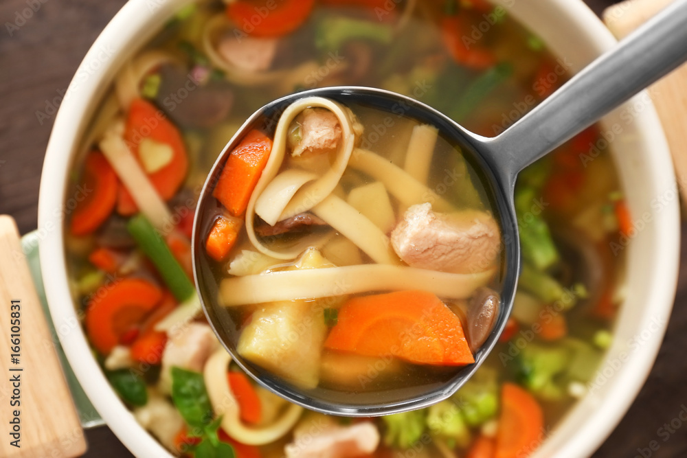 Ladle with turkey soup over saucepan, close up