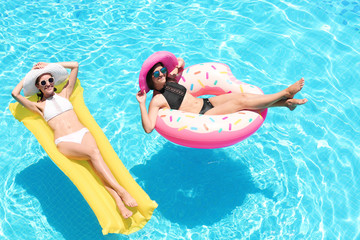 Wall Mural - Beautiful young women with inflatable donut and mattress in blue swimming pool