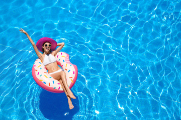 Beautiful young woman with inflatable donut in blue swimming pool