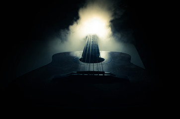 Music concept. Acoustic guitar isolated on a dark background under beam of light with smoke with copy space. Guitar Strings, close up. Selective focus. Fire effects