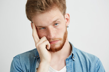 Wall Mural - Close up of bored tired young man looking at camera holding finger on temple over white background.